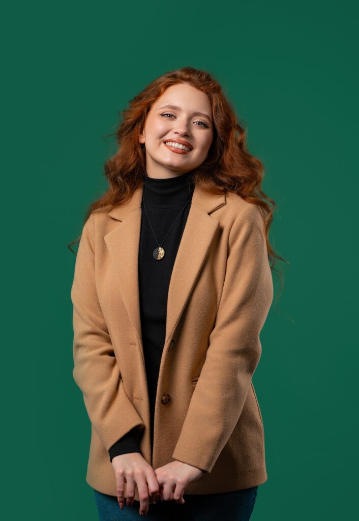 Friendly woman, red curly hair on green studio background.Smiling business lady
